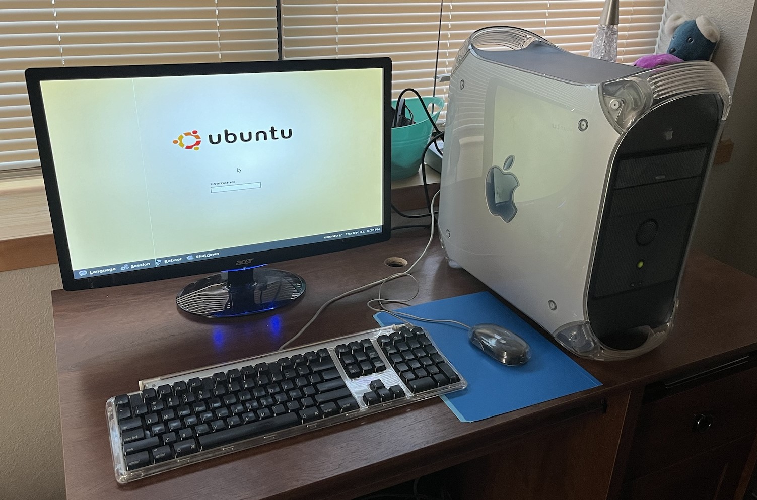 A Power Mac G4, Apple keyboard and mouse, and Acer LCD monitor sit atop a simple desk. The Power Mac G4 is powered on. Ubuntu 4.10’s login screen is shown on the monitor.